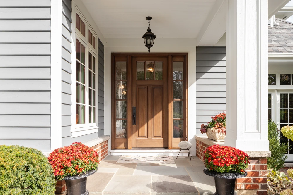 Une porte d'entrée et porche couvert détail sur une maison avec parement gris, garniture blanche, brique rouge, une porte d'entrée en bois