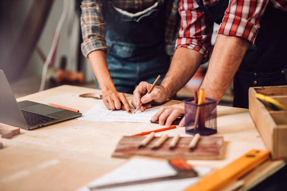 Atelier de menuiserie avec deux artisans collaborant sur des plans techniques
