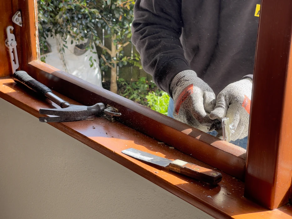 Un travailleur peint avec une brosse autour d'une fenêtre pendant que les clients supervisent le travail