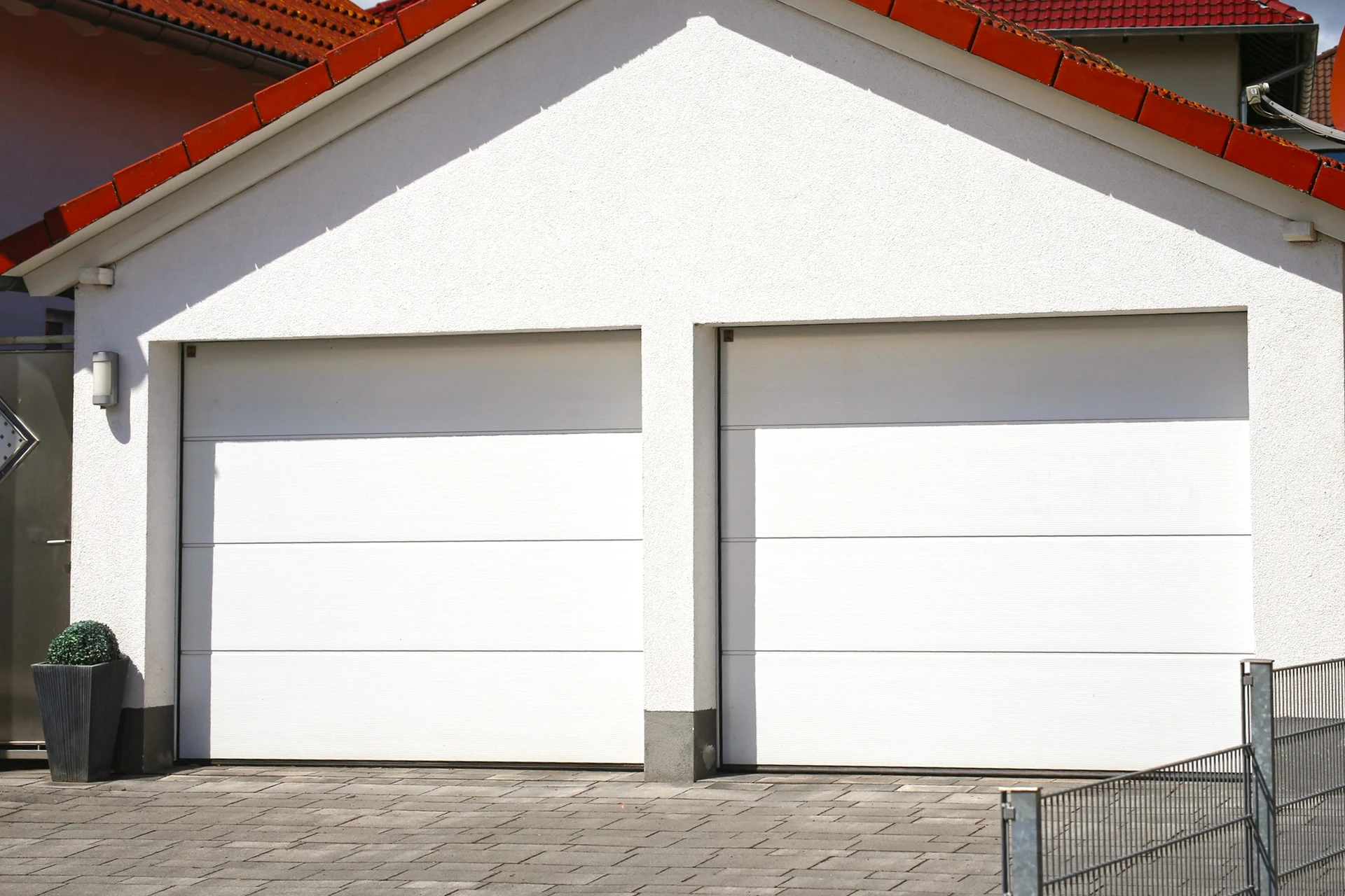Façade extérieure de garage résidentiel avec deux portes sectionnelles blanches à panneaux horizontaux lisses